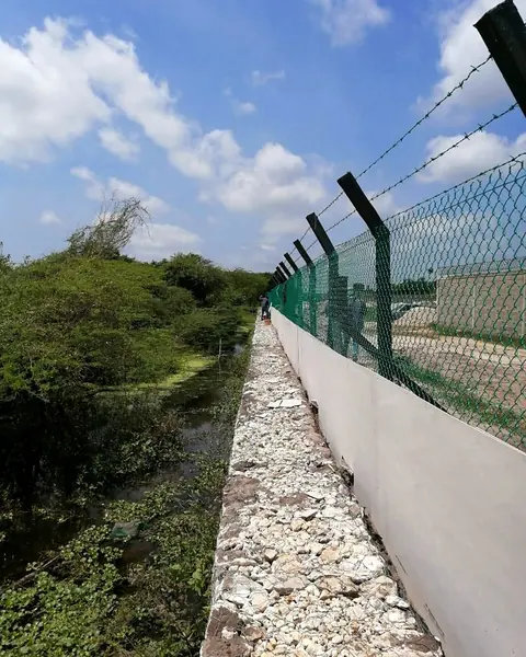 Cerramiento junto a cuerpo de agua — Zócalo y malla verde sobre borde de canal — Metalworks Energy